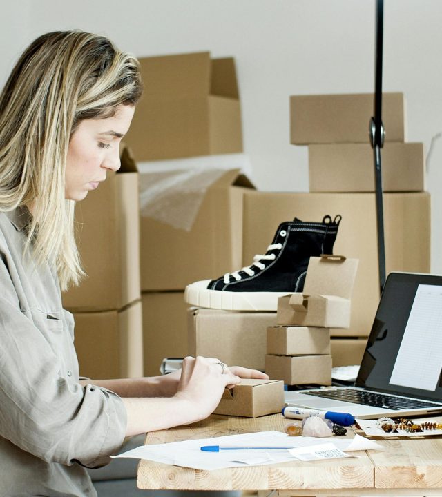 A woman packing boxes for her online store, surrounded by packaging materials and a laptop.